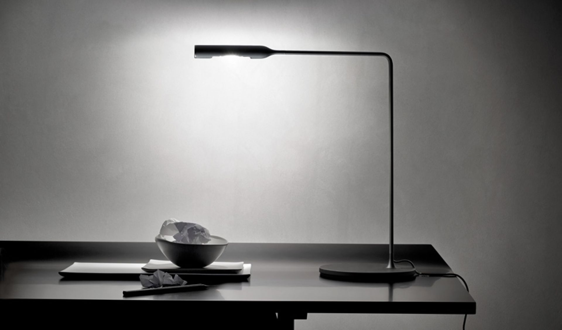 Schwarze Flo Desk Tischleuchte Lumina auf einem Schreibtisch, minimalistisches Design mit indirektem Licht.