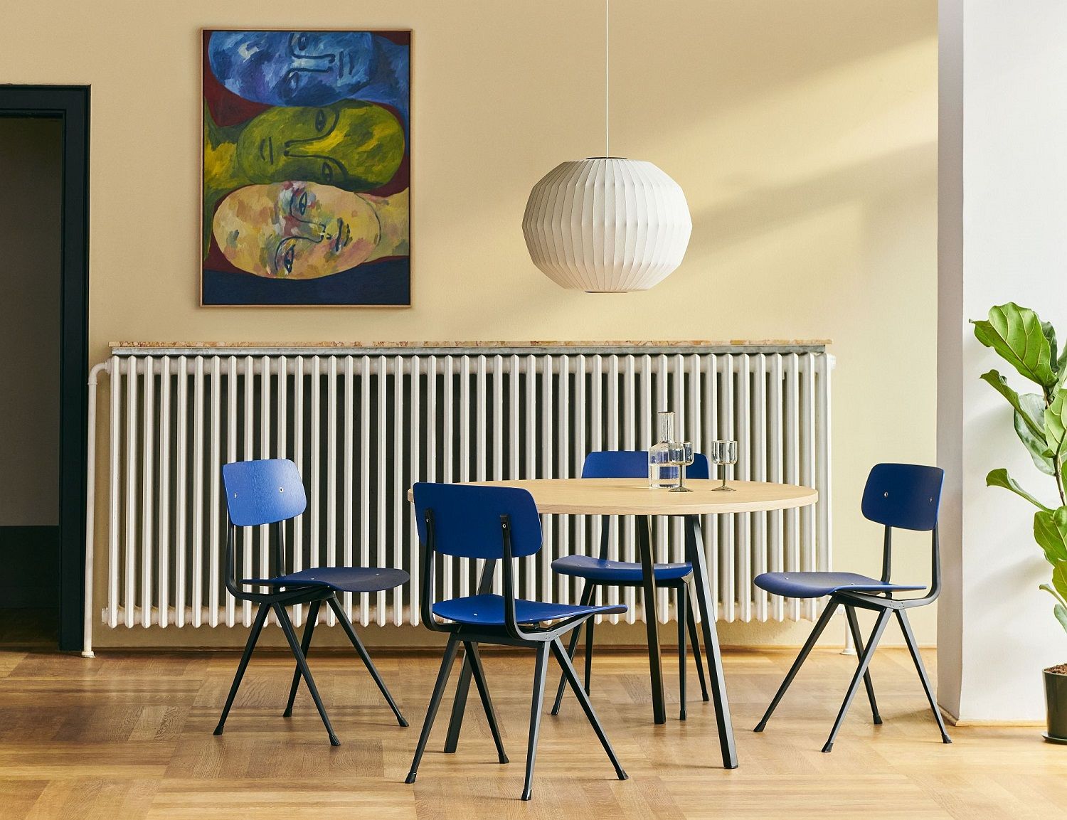 Heller Raum mit Hay Loop Stand Table Round Esstisch aus Holz, umgeben von blauen Stühlen.