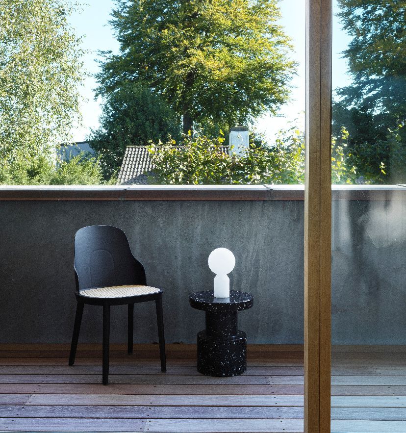 Normann Copenhagen Yo Lamp Small Akkuleuchte auf schwarzem Beistelltisch neben Stuhl auf Holzterrasse.
