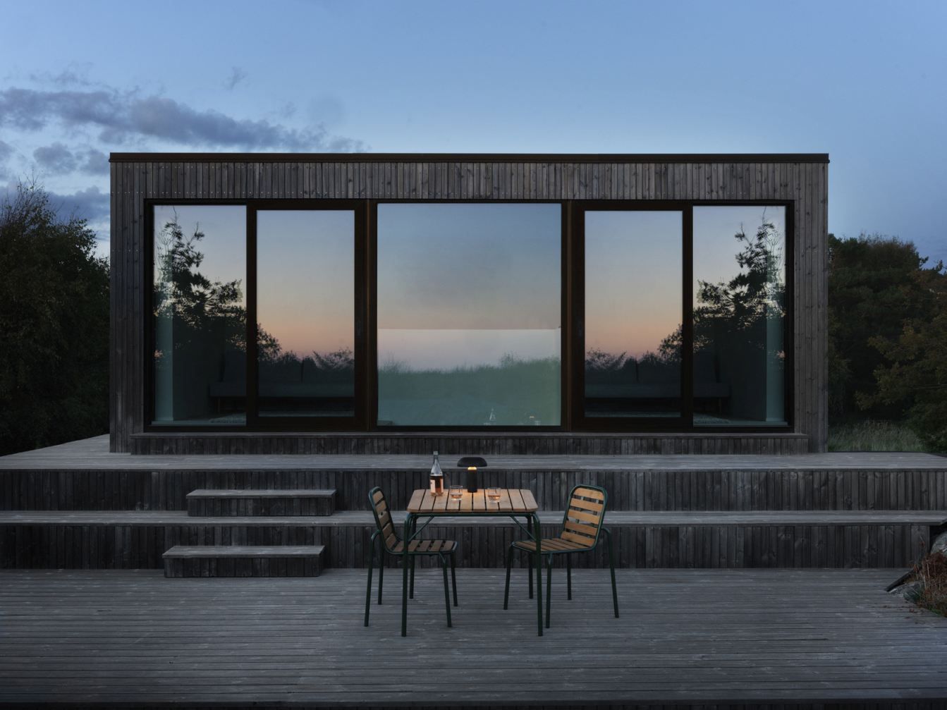 Zwei Vig Chair Wood Stühle von Normann Copenhagen auf einer Holzterrasse vor einem modernen Holzhaus.
