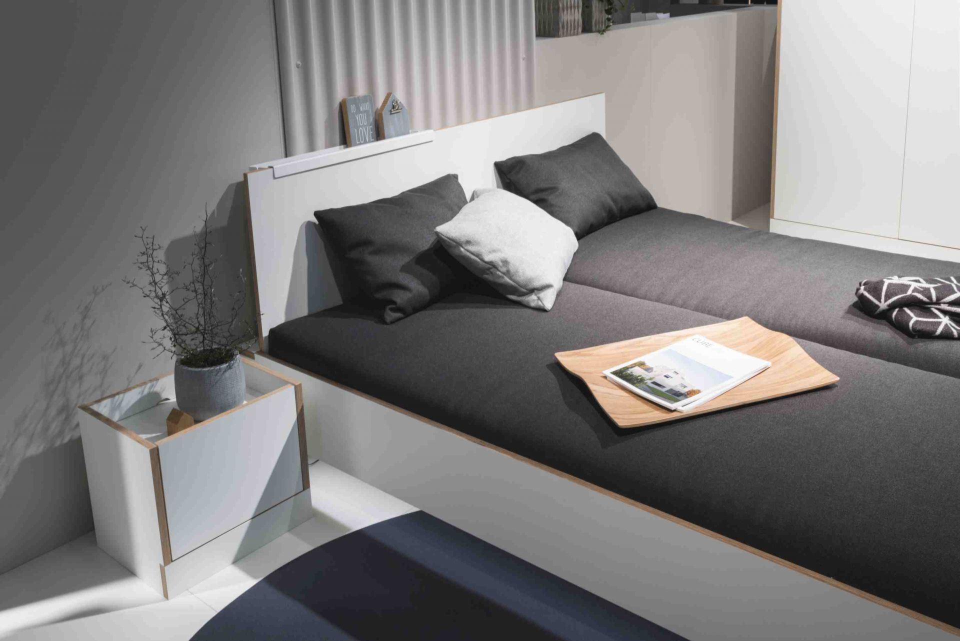 Weißes Flai Bett von Müller Möbelwerkstätten mit grauer Matratze und Nachttisch. Modernes Schlafzimmer Design.
