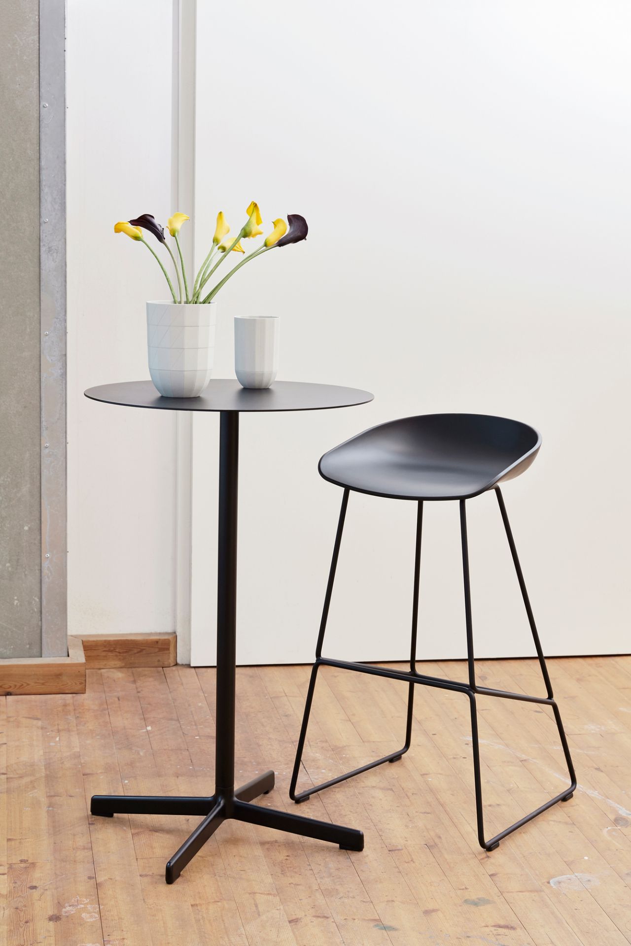 Schwarzer About a Stool AAS 38 Barhocker von Hay neben einem schwarzen Stehtisch mit Blumen.