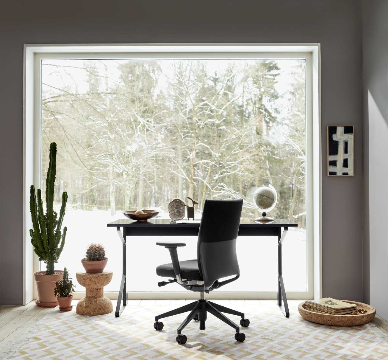 Moderner Arbeitsplatz mit Vitra ID Chair Bürodrehstuhl, schwarzem Schreibtisch und Blick auf verschneite Winterlandschaft.