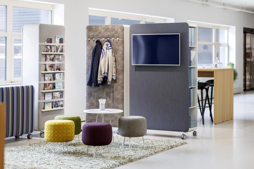 Büro mit Cascando Pillow Space Akustik-Raumteilern: Stellwand mit Bildschirm, Garderobe, Zeitschriftenregal und farbigen Hockern.