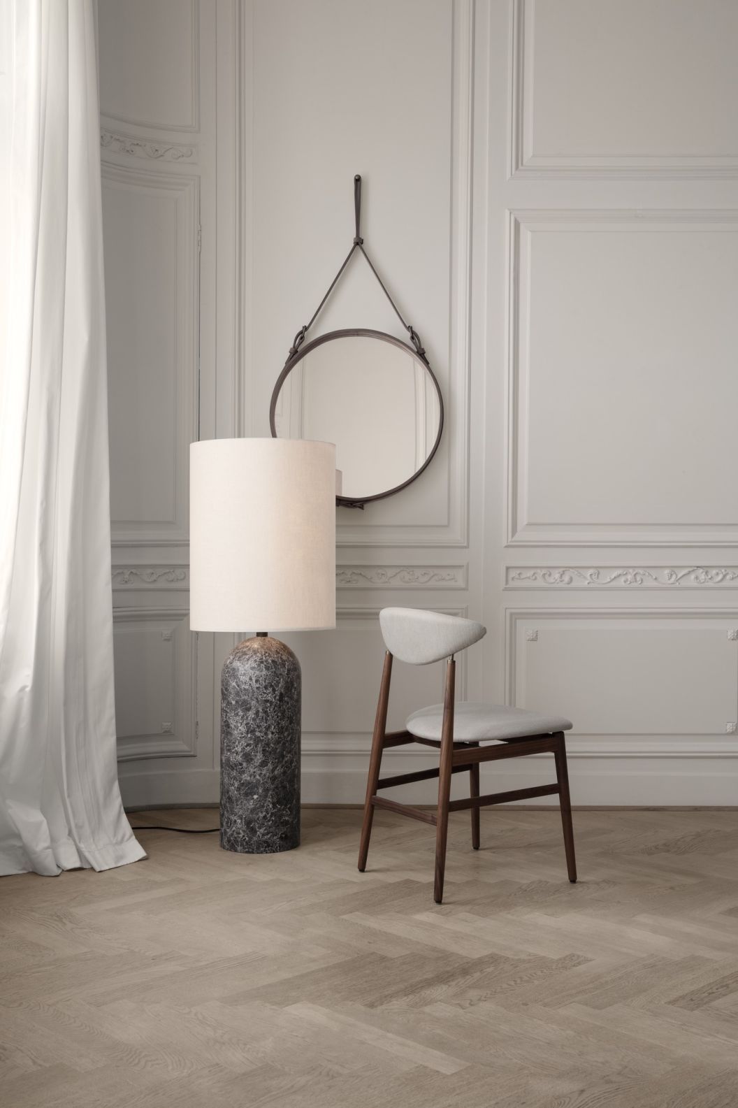 Gubi Adnet runder Wandspiegel mit Lederriemen, Stehlampe und Stuhl in einem stilvollen Interieur.