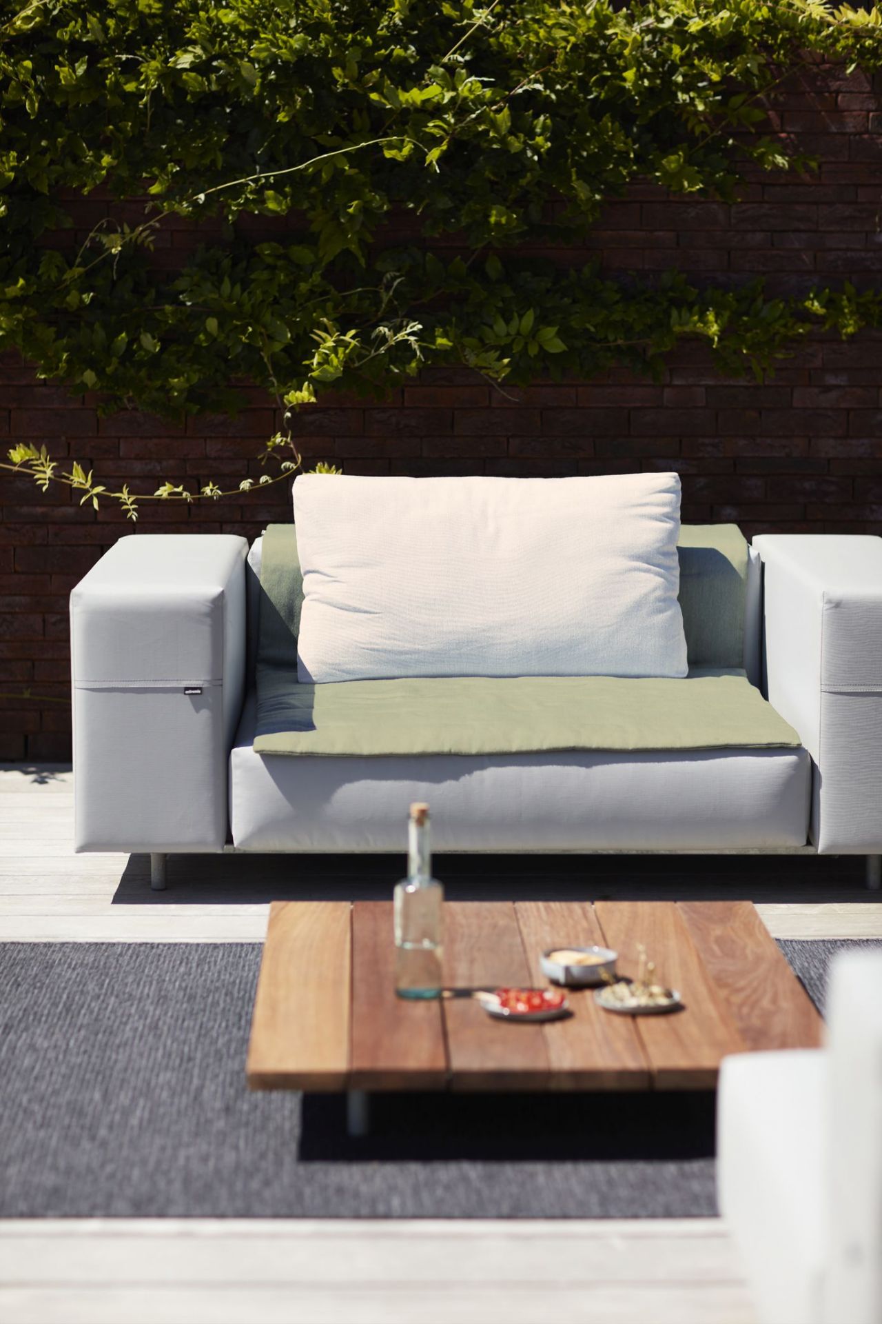 Walrus Outdoor Club Sessel von Extremis, graues Lounge-Sofa mit Kissen und Holztisch im Garten.
