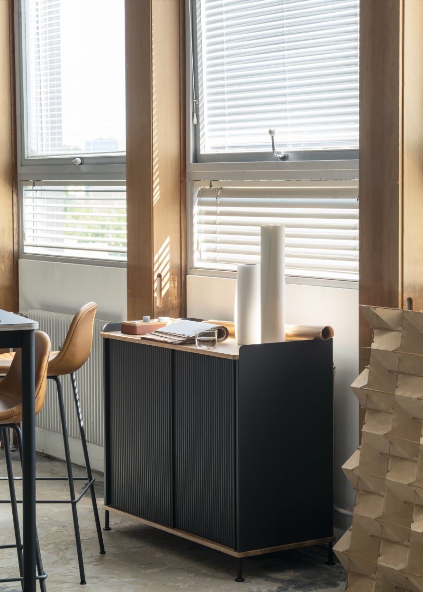 Muuto Arrange Desktop Serie Konfiguration 1: Schwarzes Sideboard mit Schiebetüren und hellen Holzdetails in einem modernen Büro.