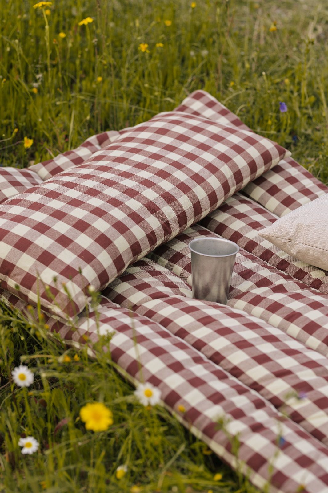 Nahaufnahme einer Ferm Living Picknickdecke mit Tumbled Cup Campingtasse im Gras.