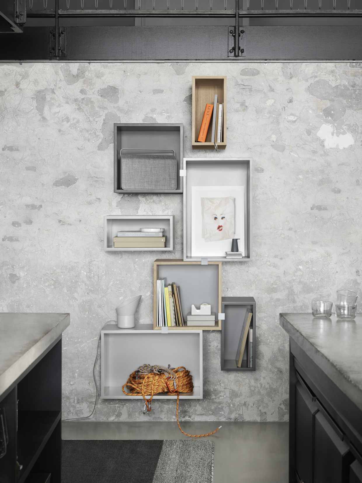 Muuto Stacked Regalsystem 2.0 an grauer Wand mit Büchern, Deko und Kletterseil.