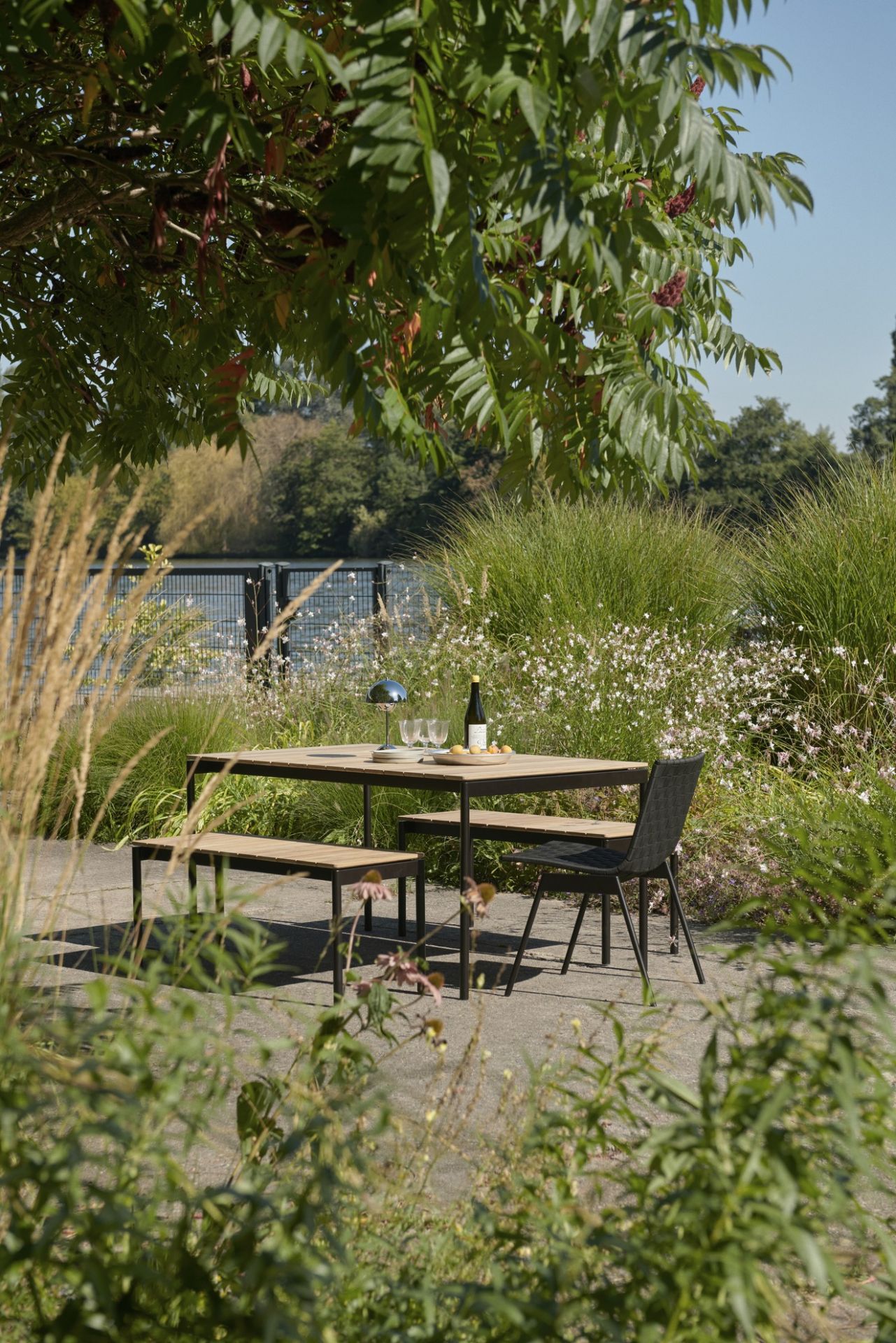AndTradition Ville AV33 Outdoor Stuhl mit passendem Gartentisch und Bank im Grünen.