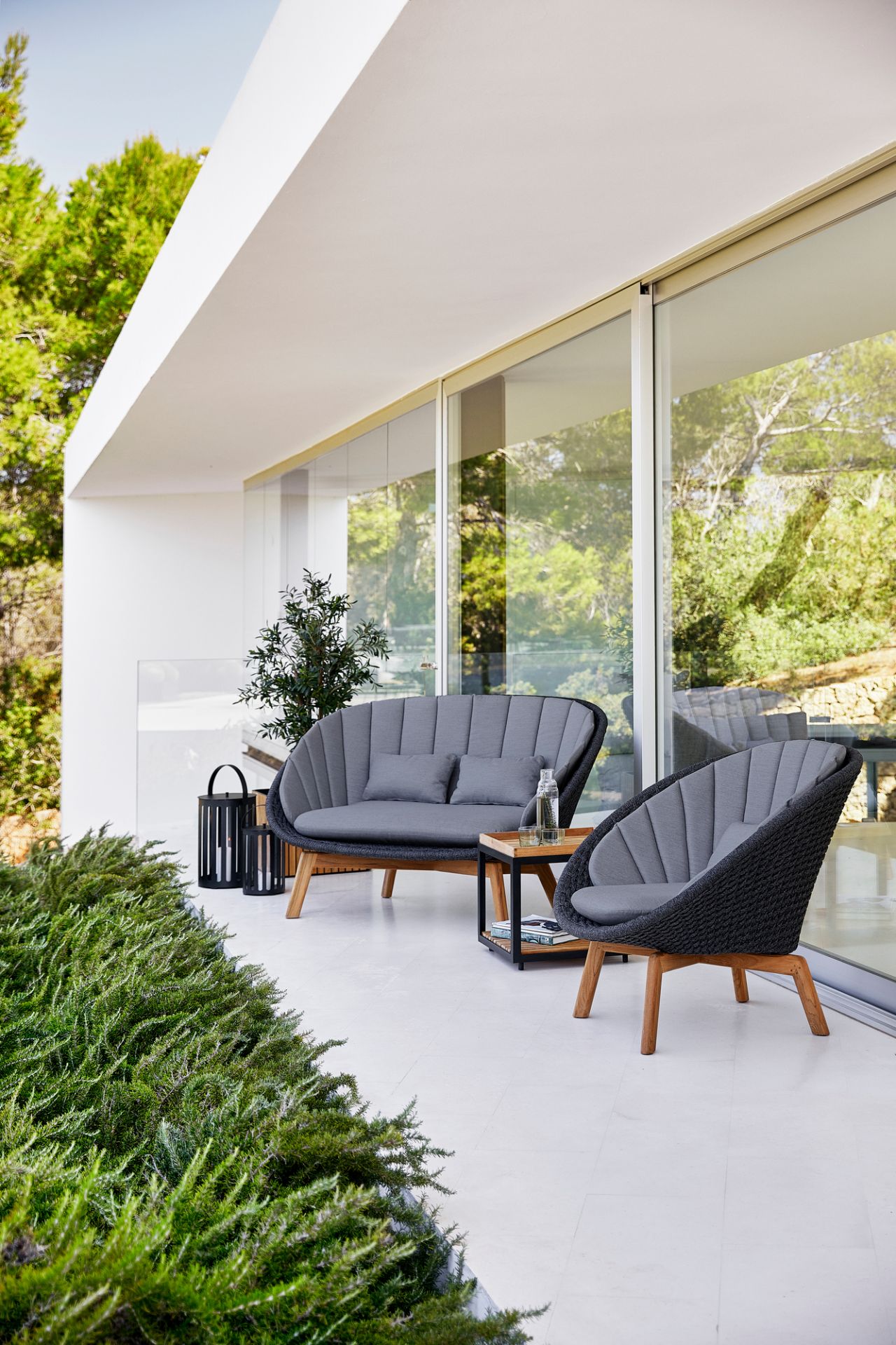 Graues Cane-Line Peacock Outdoor Sofa und Sessel auf einer Terrasse mit Tisch und Dekoration.