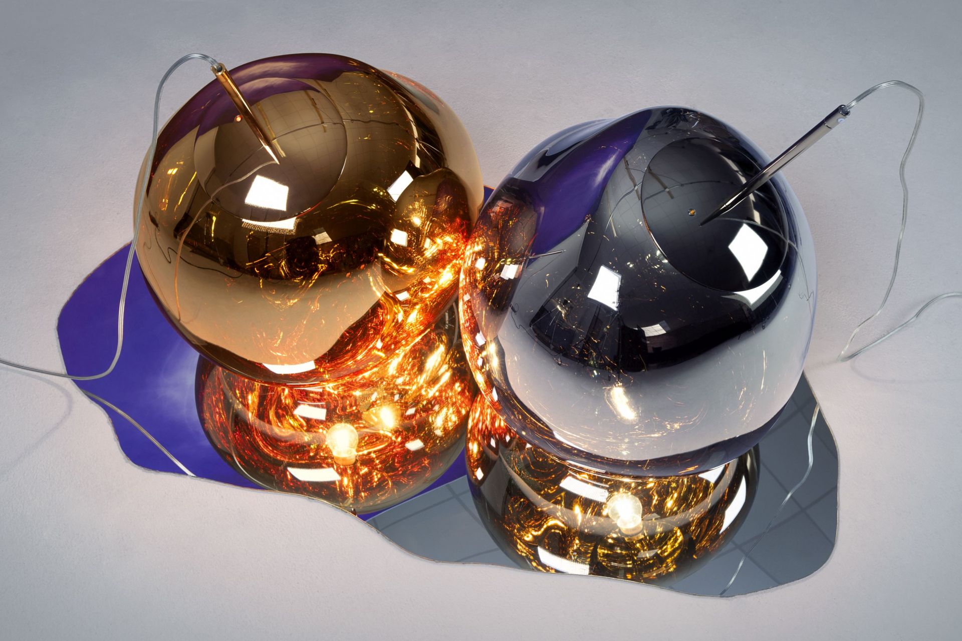 Nahaufnahme von zwei Tom Dixon Melt LED Pendelleuchten in Gold und Chrom mit warmem Licht.
