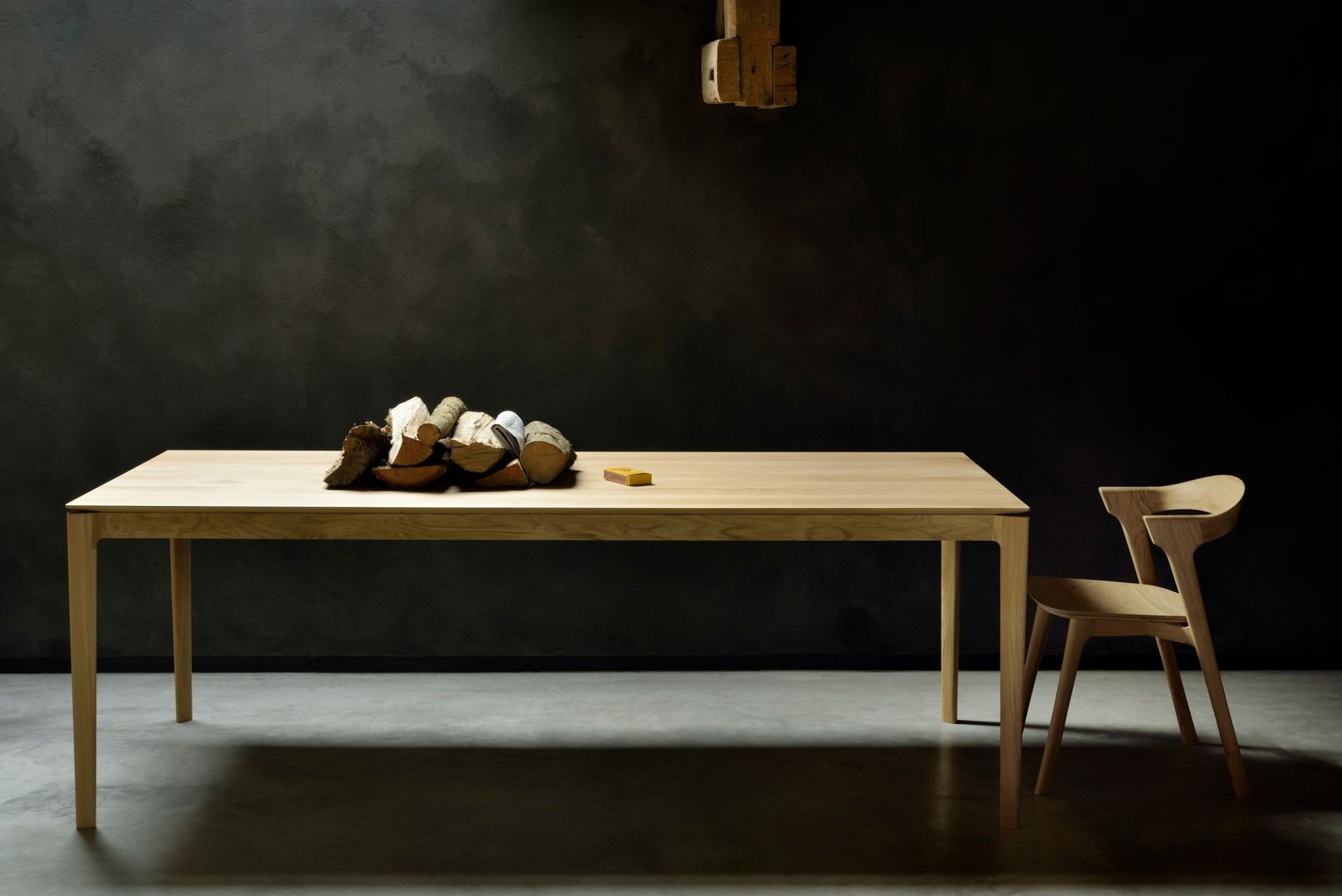 Bok Esstisch aus Eiche von Ethnicraft mit Stuhl und Holzscheiten im minimalistischen Interieur.