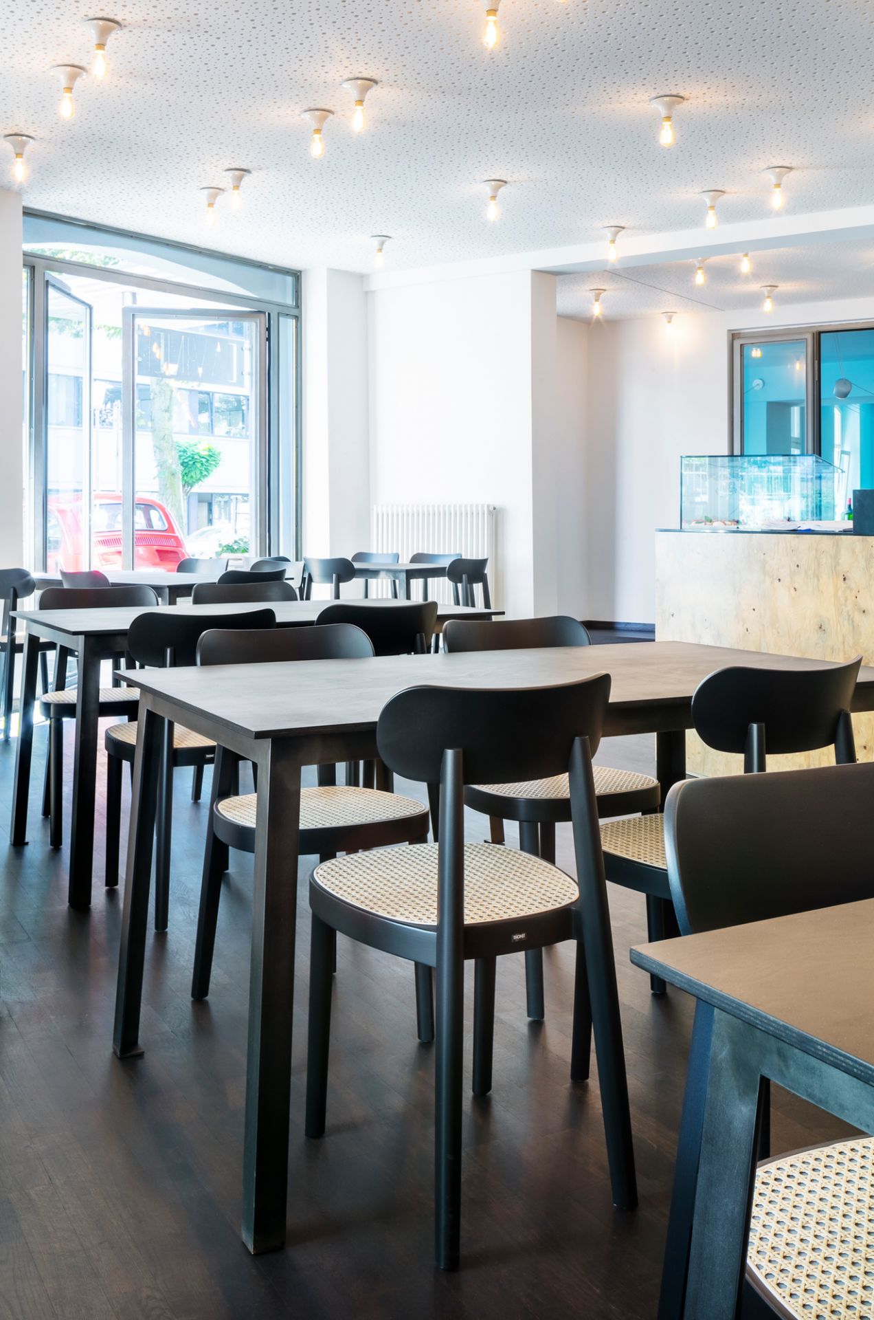 Innenaufnahme eines Restaurants mit mehreren schwarzen Holzstühlen vom Typ Thonet 118 mit Wiener Geflecht.