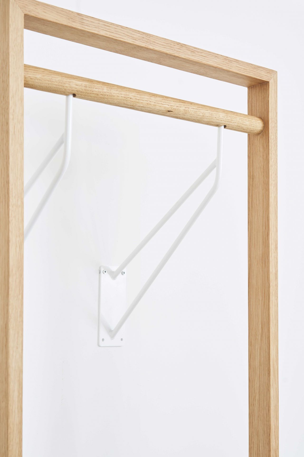 Nahaufnahme der gardero-b Wandgarderobe: Helles Holzgestell mit weißer Kleiderstange und Wandbefestigung. Keywords: Garderobe, Wandgarderobe, Holz, Design.
