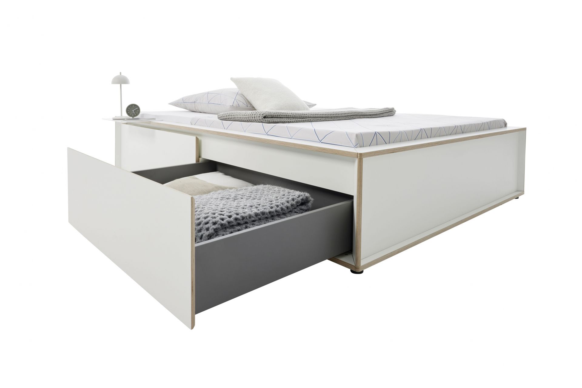 Spaze Bett von Müller Möbelwerkstätten mit Schublade, Nachttisch, Lampe, Kissen und Decke.