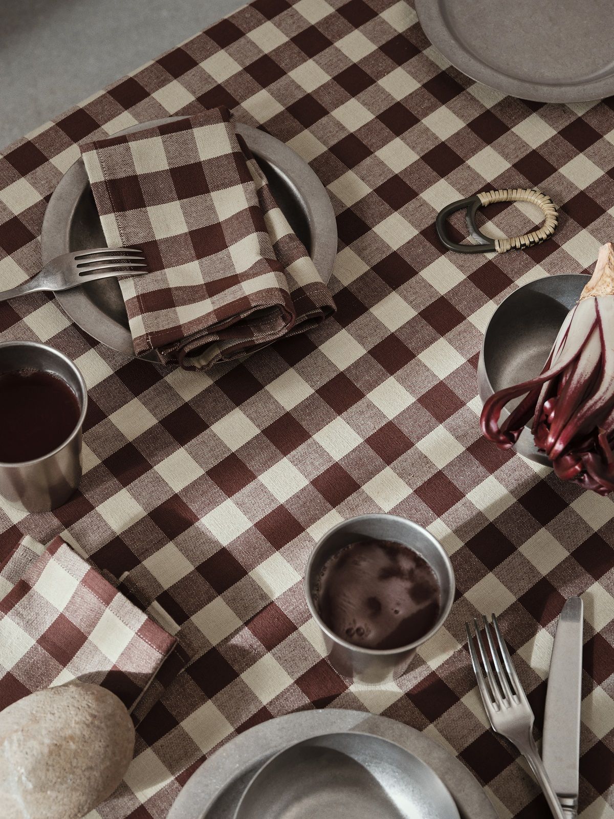 Nahaufnahme eines Picknicktisches mit Ferm Living Tumbled Cup, Geschirr und rot-weiß karierter Tischdecke.