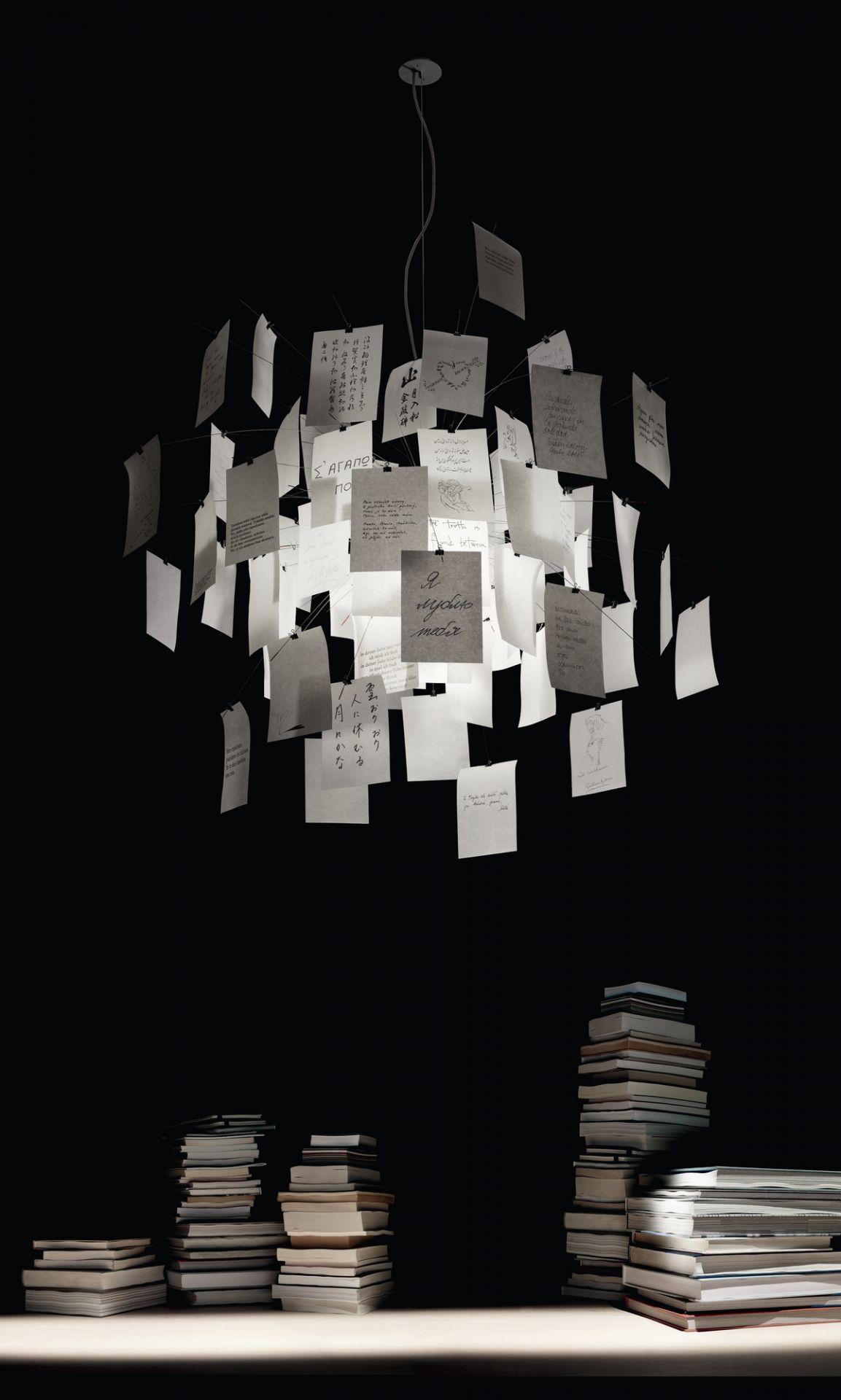 Zettel'z 5 Hängeleuchte von Ingo Maurer, moderne Designerlampe mit beschrifteten Zetteln, Bücherstapel im Vordergrund, stimmungsvolle Beleuchtung.