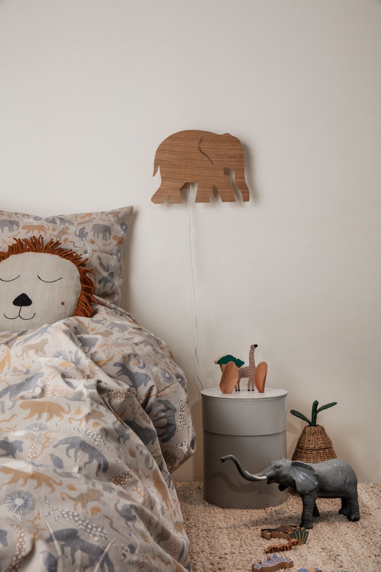 Kinderzimmer-Szene mit Ferm Living Aufbewahrungskorb (ähnlich Birne) neben Bett mit Tiermotiven und Holzspielzeug.