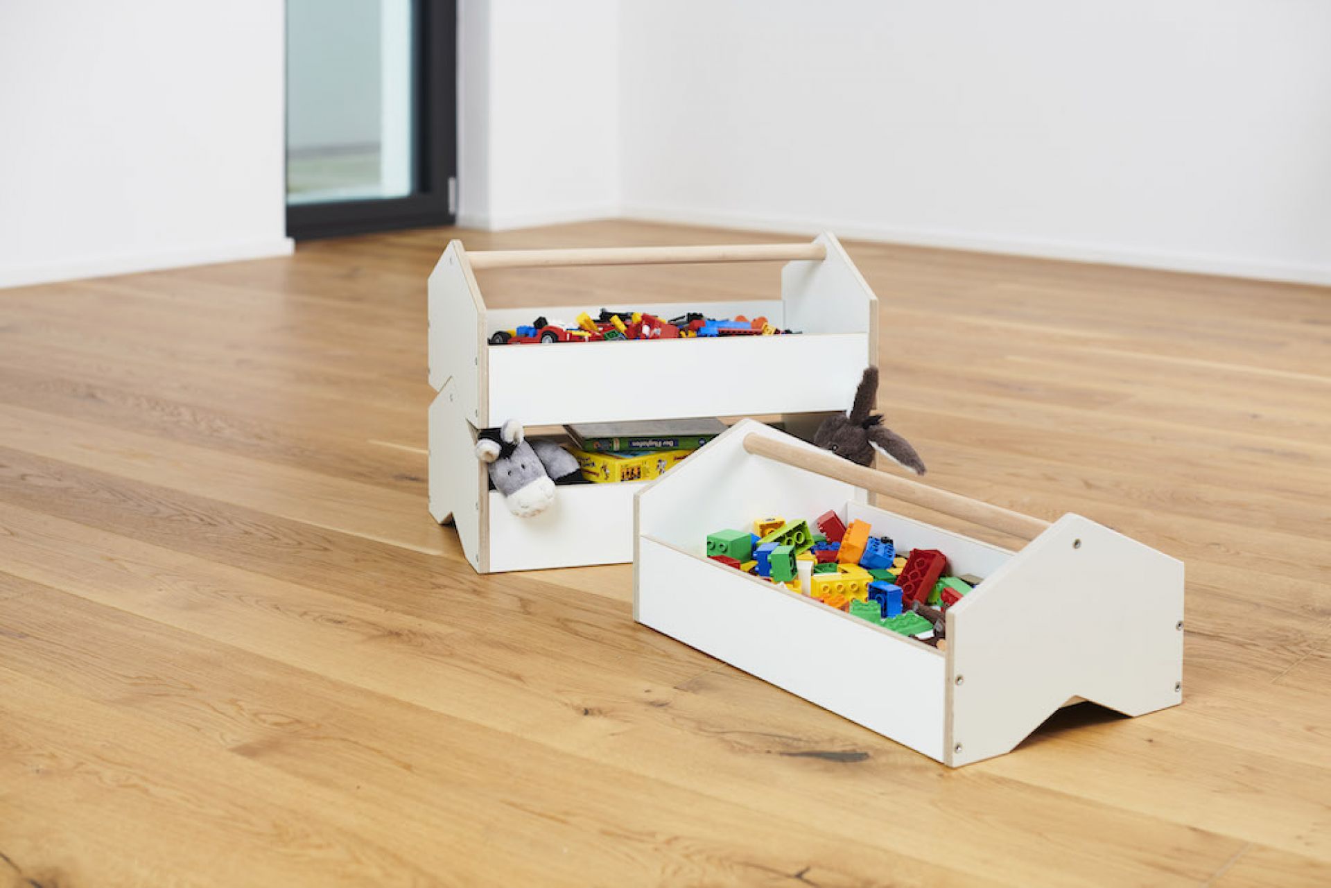 Tojo Kids Werkzeugkiste: Zwei weiße Spielzeugkisten aus Holz, gefüllt mit Spielzeug und Kuscheltieren, auf Holzboden.