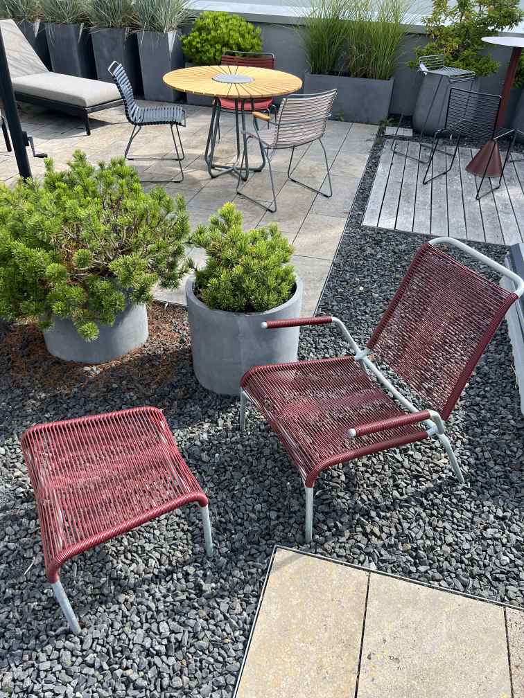 Altofer Lounge Sessel mit Hocker, Outdoor Sitzmöbel aus rotem Kunststoffgeflecht und silbernem Gestell auf Kies.