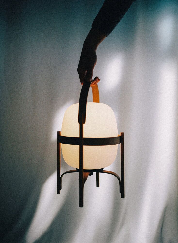 Hand hält Cestita Batería Akkuleuchte von Santa & Cole, moderne Tischlampe mit warmem Licht.