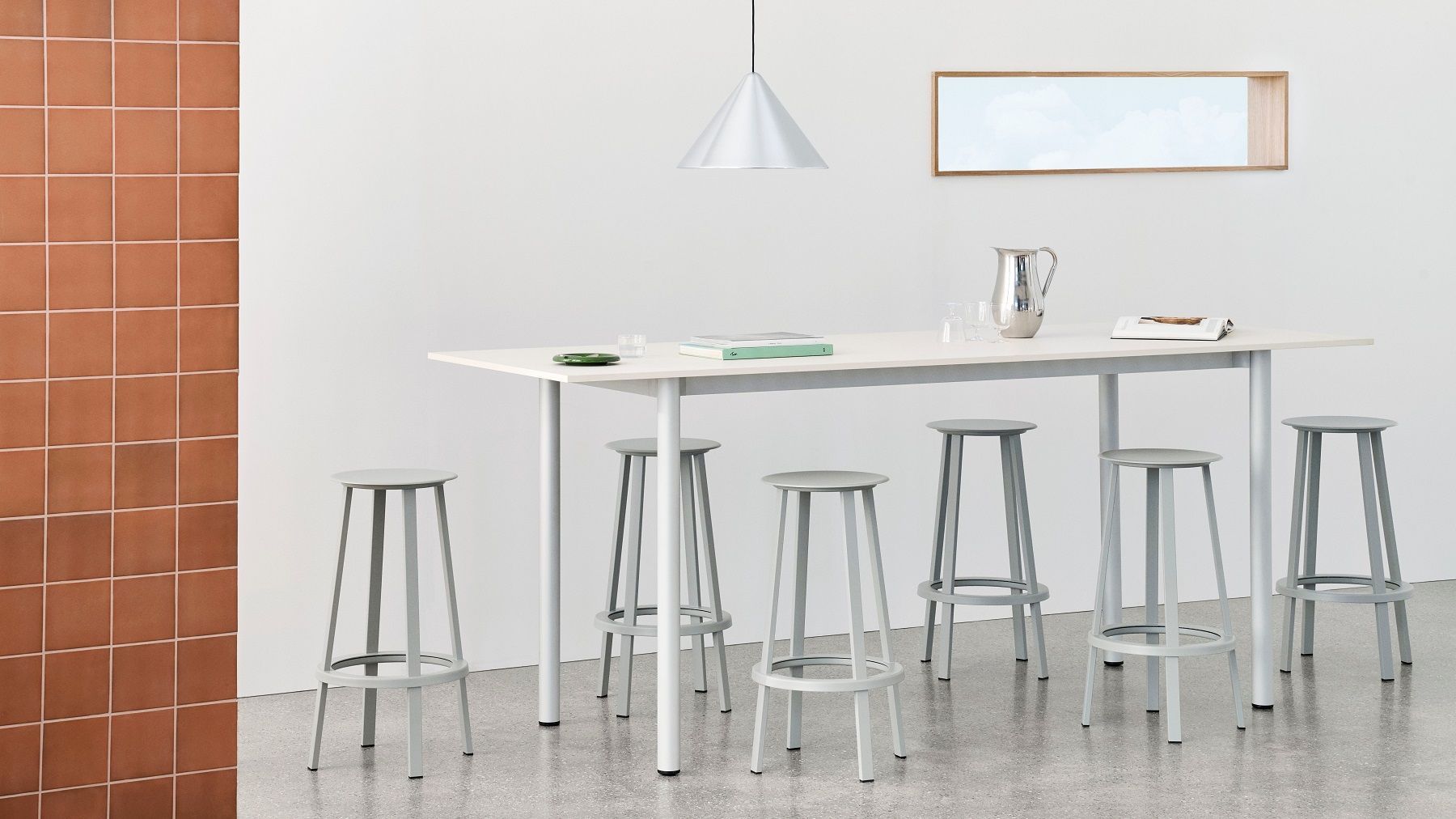 Helle Küche mit Hay Compass Pendelleuchte aus gebürstetem Aluminium über einem weißen Tisch mit grauen Hockern.