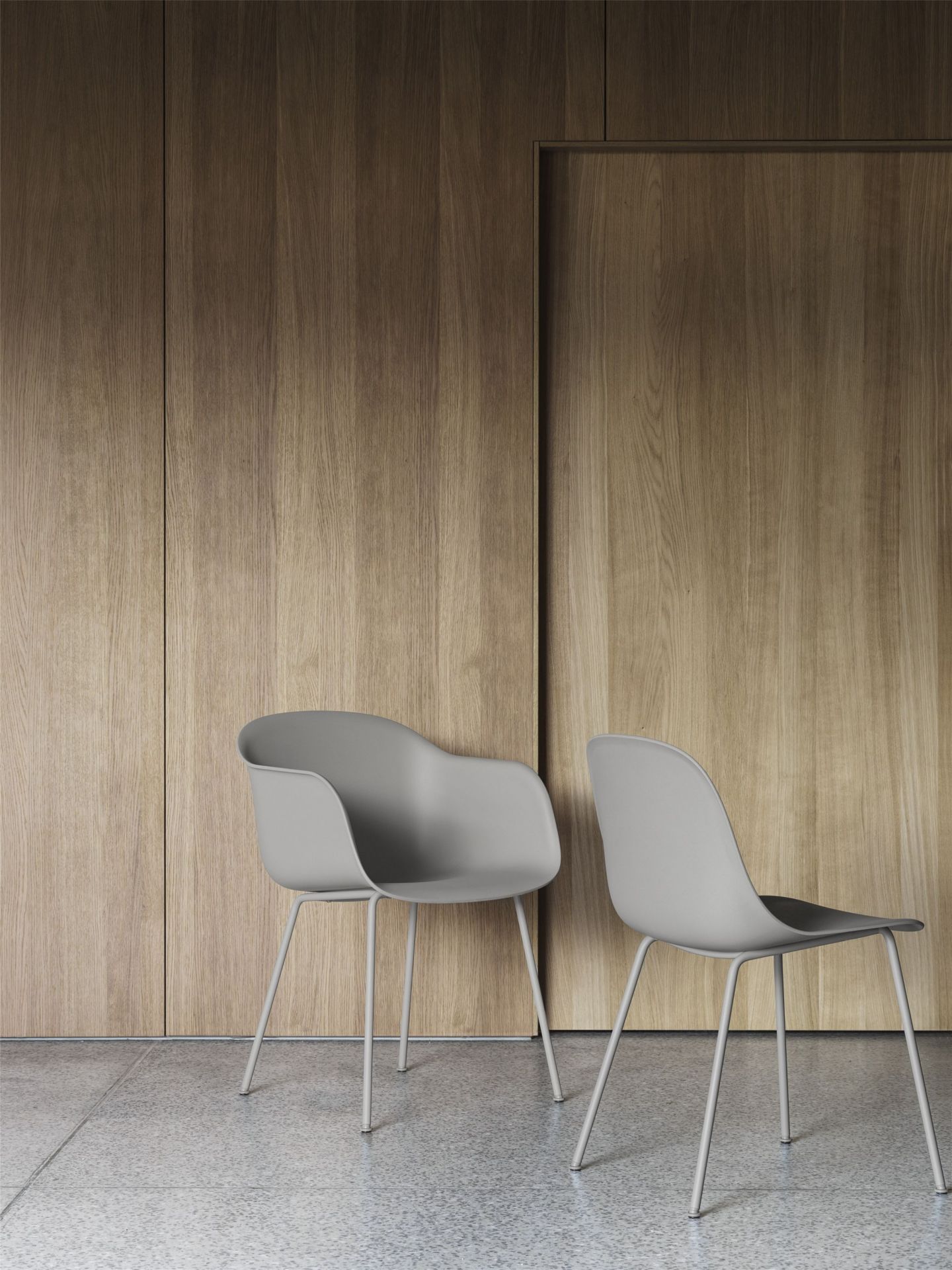 Zwei graue Fiber Armchair Stühle von Muuto mit Stahlrohrgestell vor einer Holzwand.