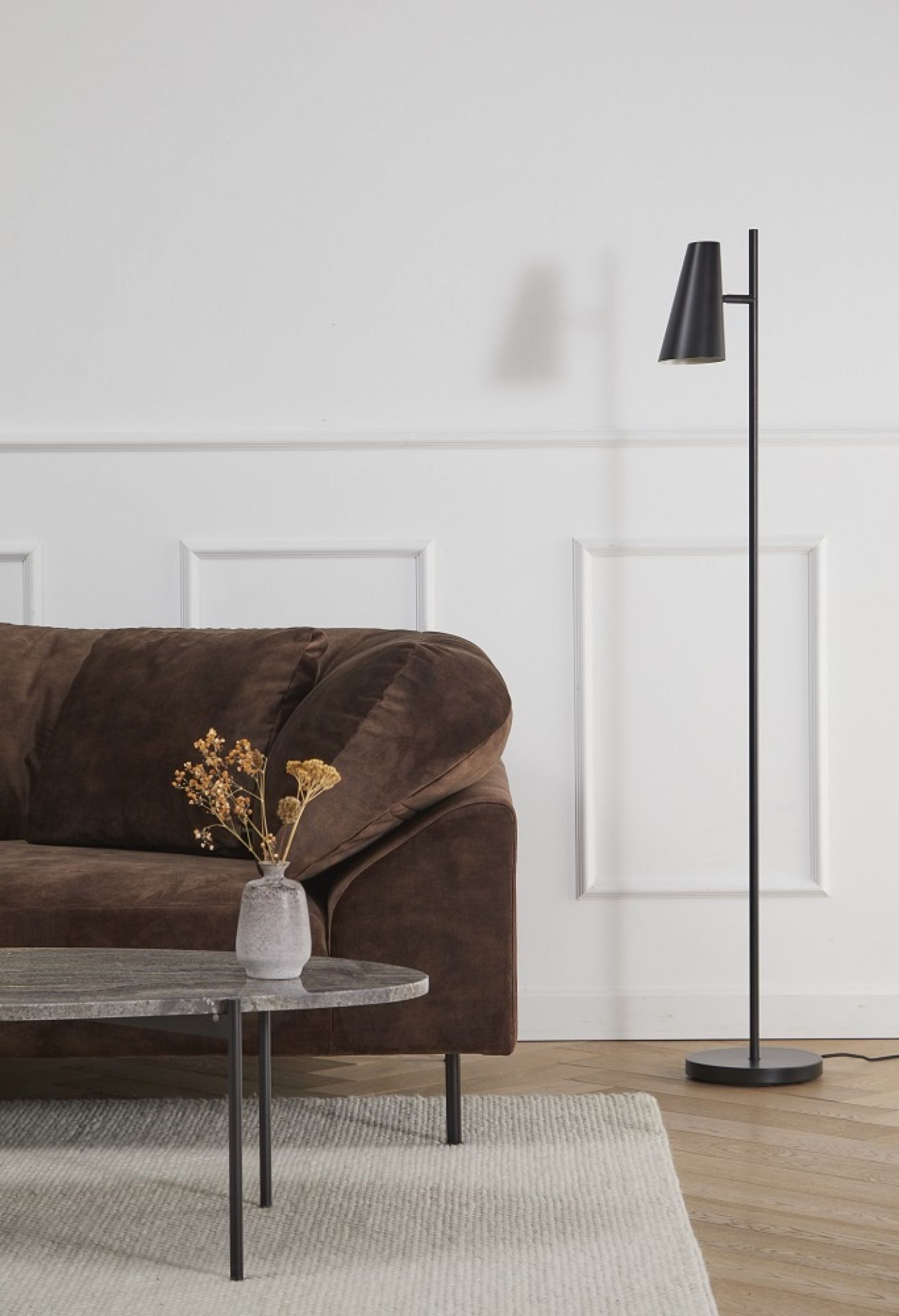 La Terra Couchtisch von Woud, oval, graue Marmorplatte, schwarzes Metallgestell, neben braunem Sofa und Stehlampe.