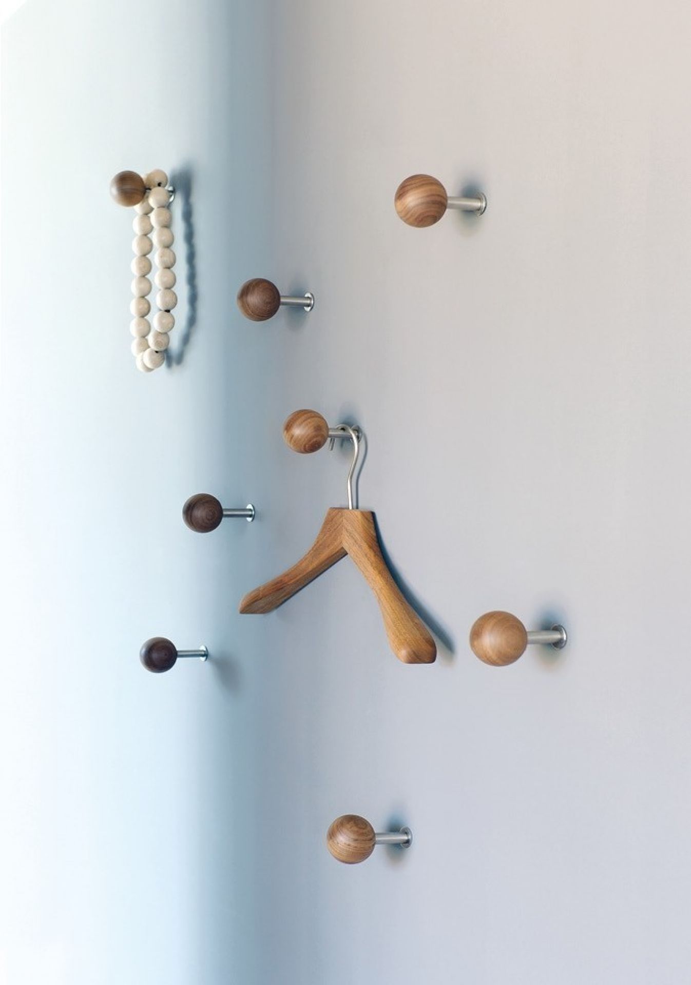 Dots Wandhaken aus Nussbaumholz an Wand befestigt, einer mit Kleiderbügel, einer mit Holzkette.