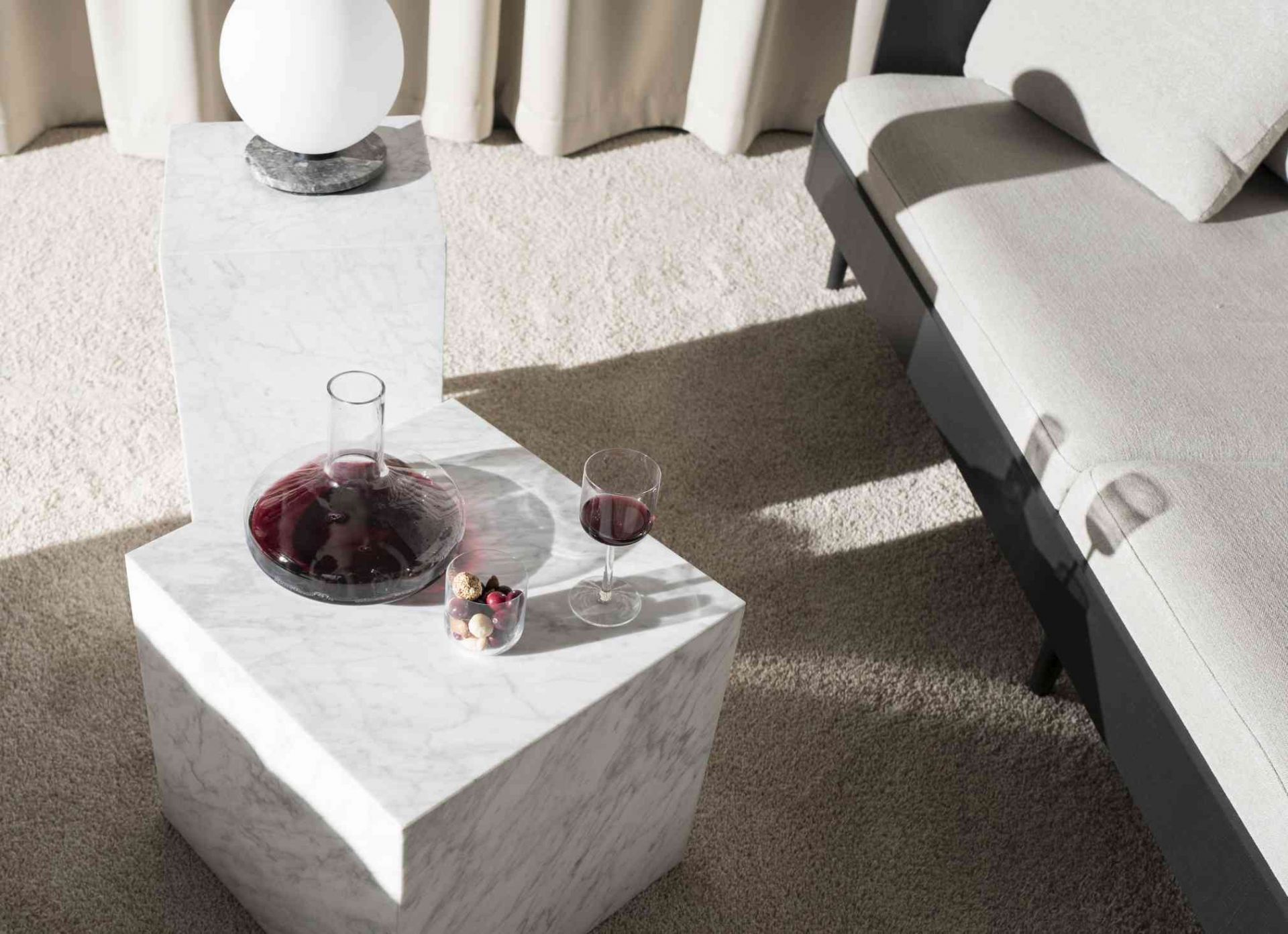 Audo Copenhagen Plinth Tisch aus Marmor mit Dekanter, Weinglas und Süßigkeiten im Wohnzimmer.