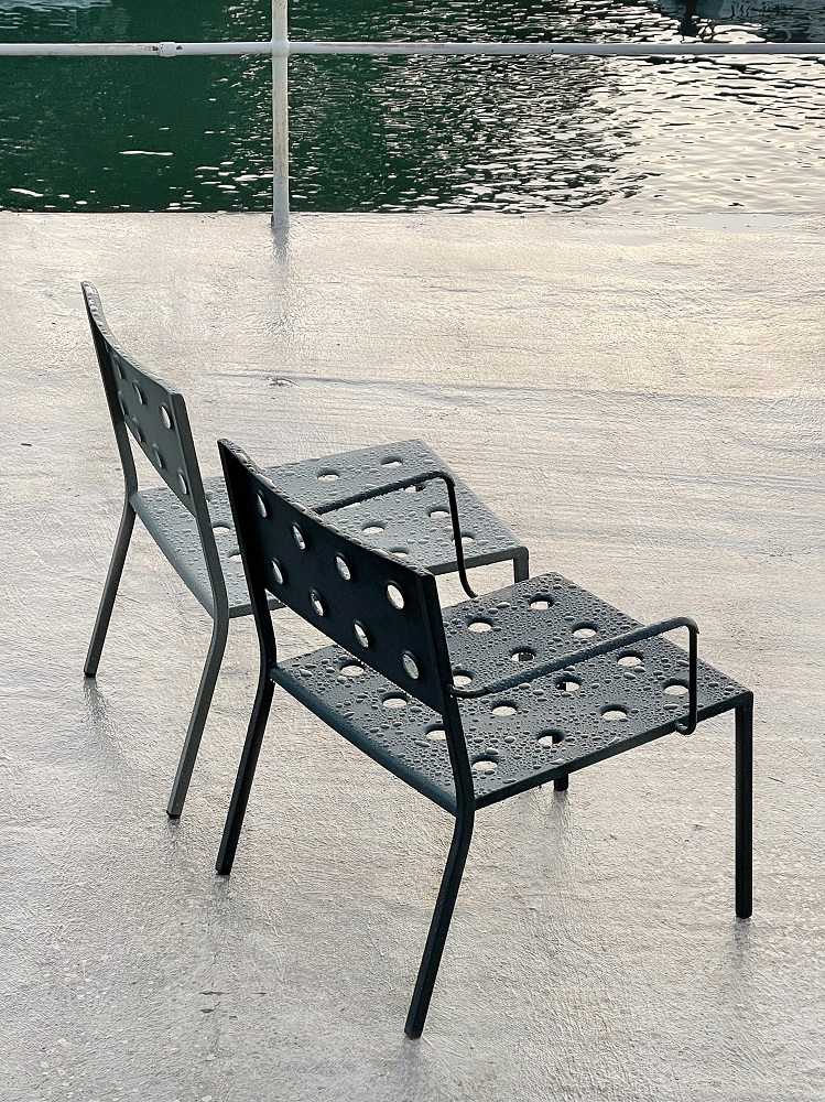 Zwei graue Hay Balcony Outdoor Lounge Stühle mit Armlehnen und Lochmuster, nass vom Regen.