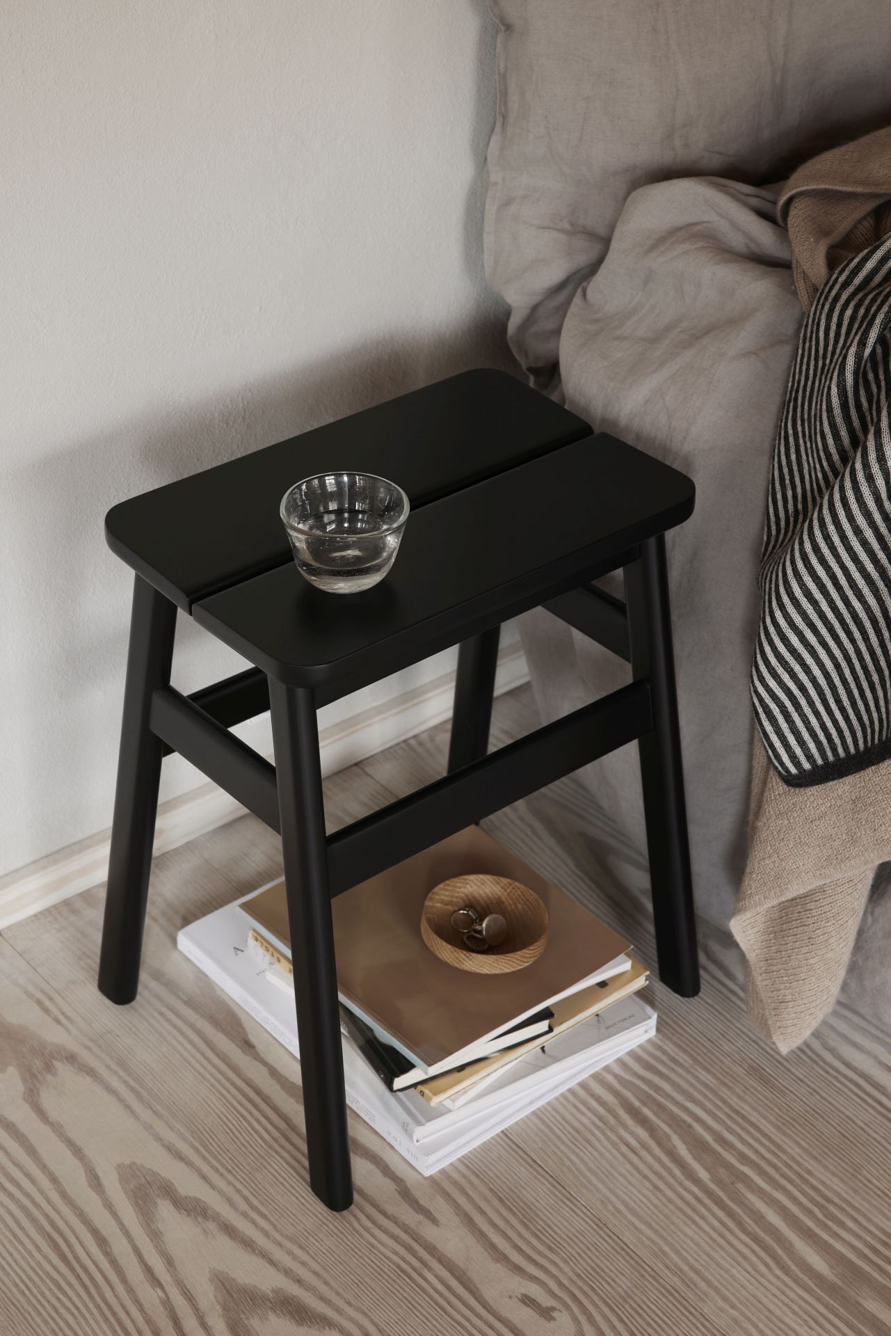 Schwarzer Angle Hocker von Form & Refine als Nachttisch mit Deko-Objekten und Büchern.