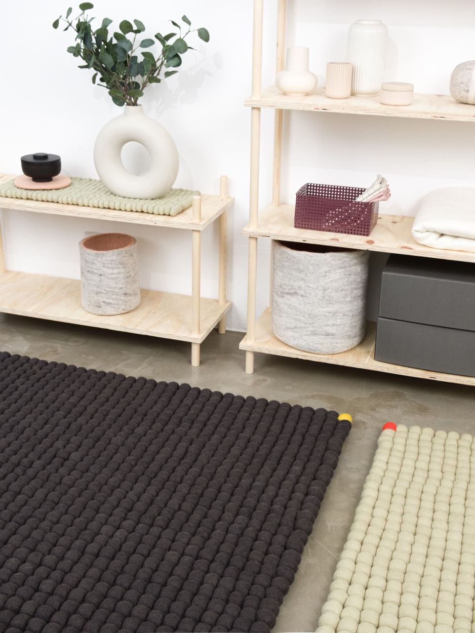 Dunkelgrauer Big One Filzteppich von myfelt (200x300 cm) im Raum, neben hellem Filzteppich und Holzregal.