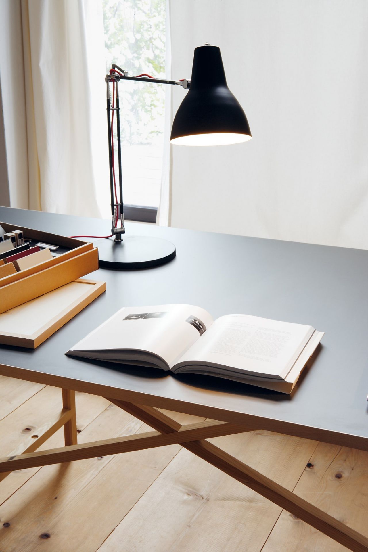 Egon Tisch von Nils Holger Moormann mit Buch, Lampe und Holzablage auf Holzboden.