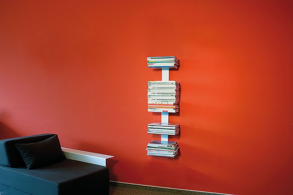 Booksbaum Wandregal: Weißes Magazinregal an roter Wand, gefüllt mit Zeitschriften und Büchern.