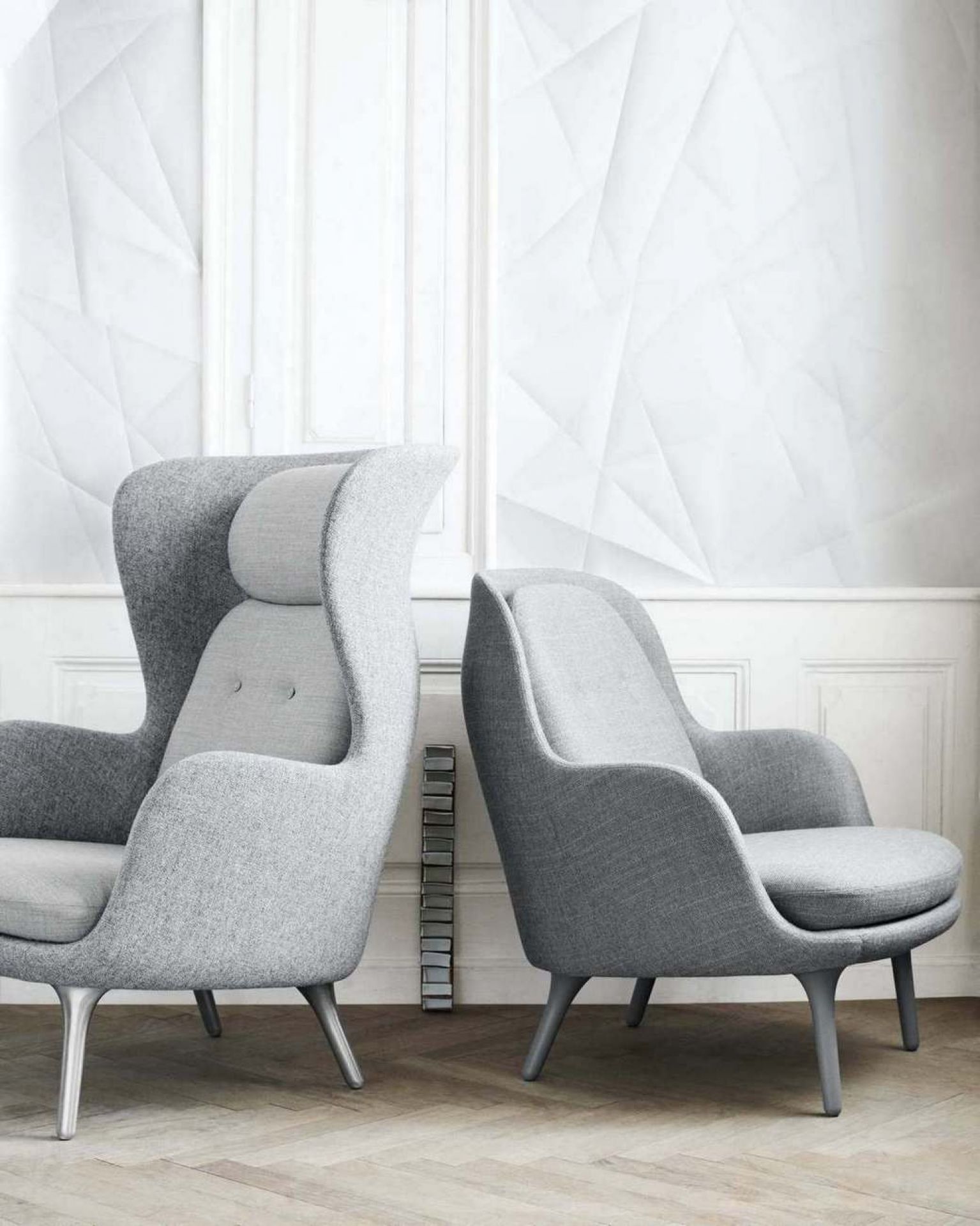 Zwei graue Fri Sessel von Fritz Hansen, ein Ohrensessel und ein Lounge Sessel, vor weißer Wand.