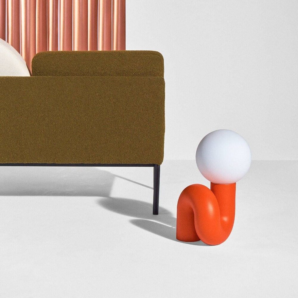 Orangefarbene Neotenic Tischleuchte von Petite Friture mit kugelförmigem Lampenschirm neben einem olivgrünen Sofa.