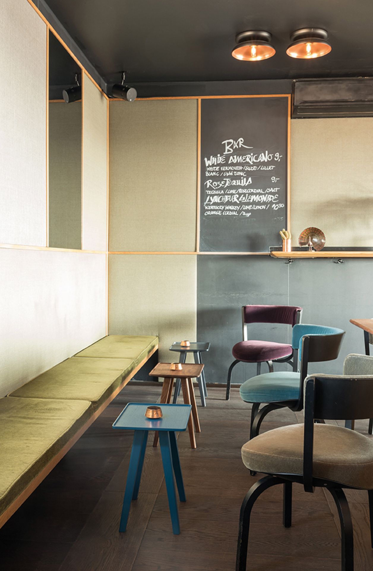 Nini Hocker Schönbuch: Bar-Interieur mit Hockern in Blau, Braun und Grau neben einer grünen Sitzbank.