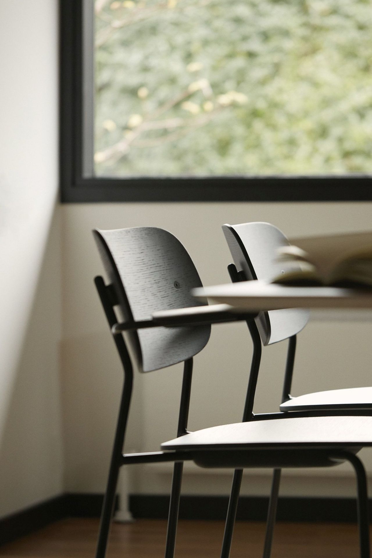 Nahaufnahme von zwei Co Dining Chairs von Audo Copenhagen mit schwarzem Metallgestell und Holzlehne.