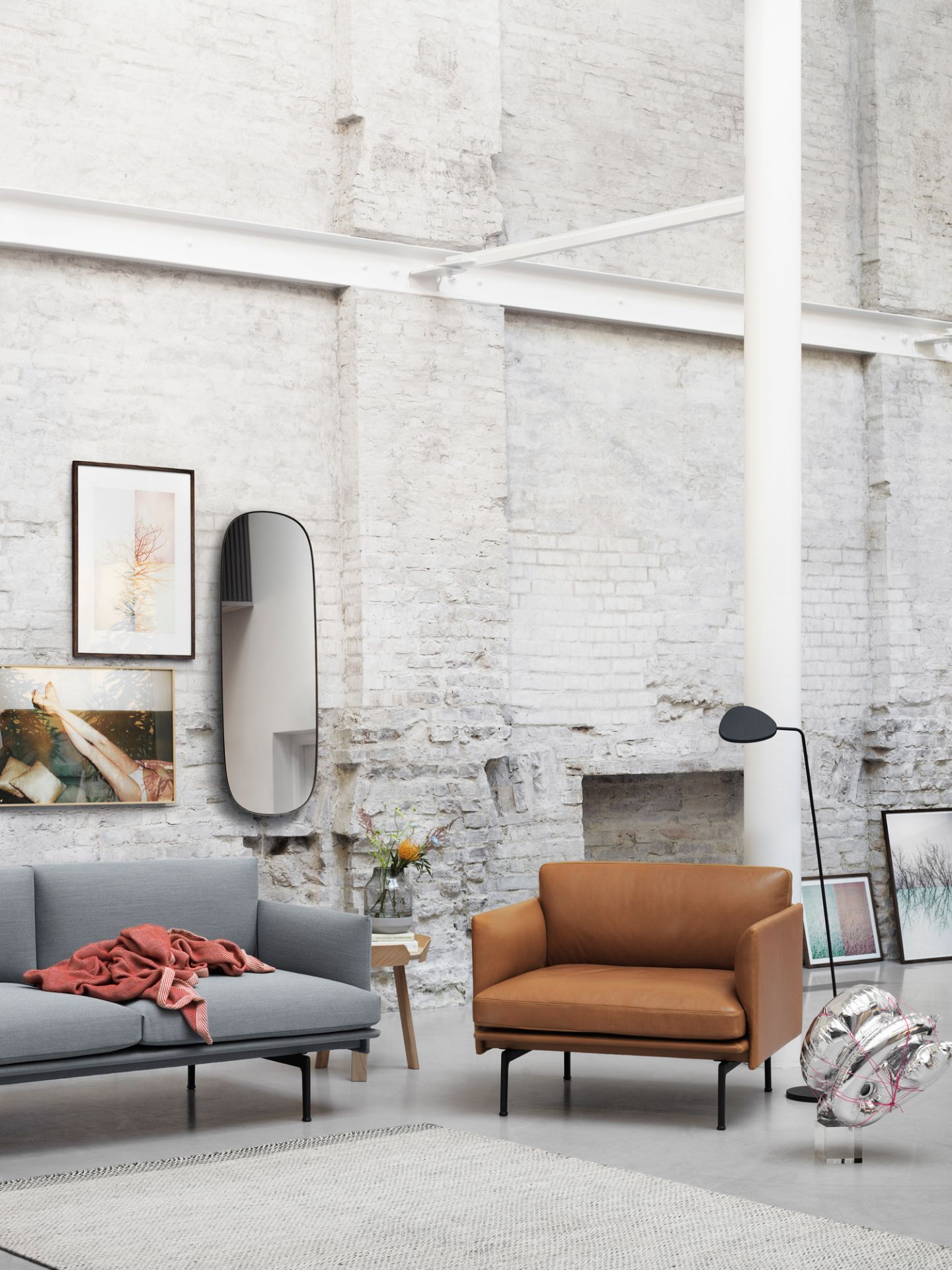 Wohnzimmer mit braunem Muuto Outline Sessel und grauem Sofa vor einer Backsteinwand.