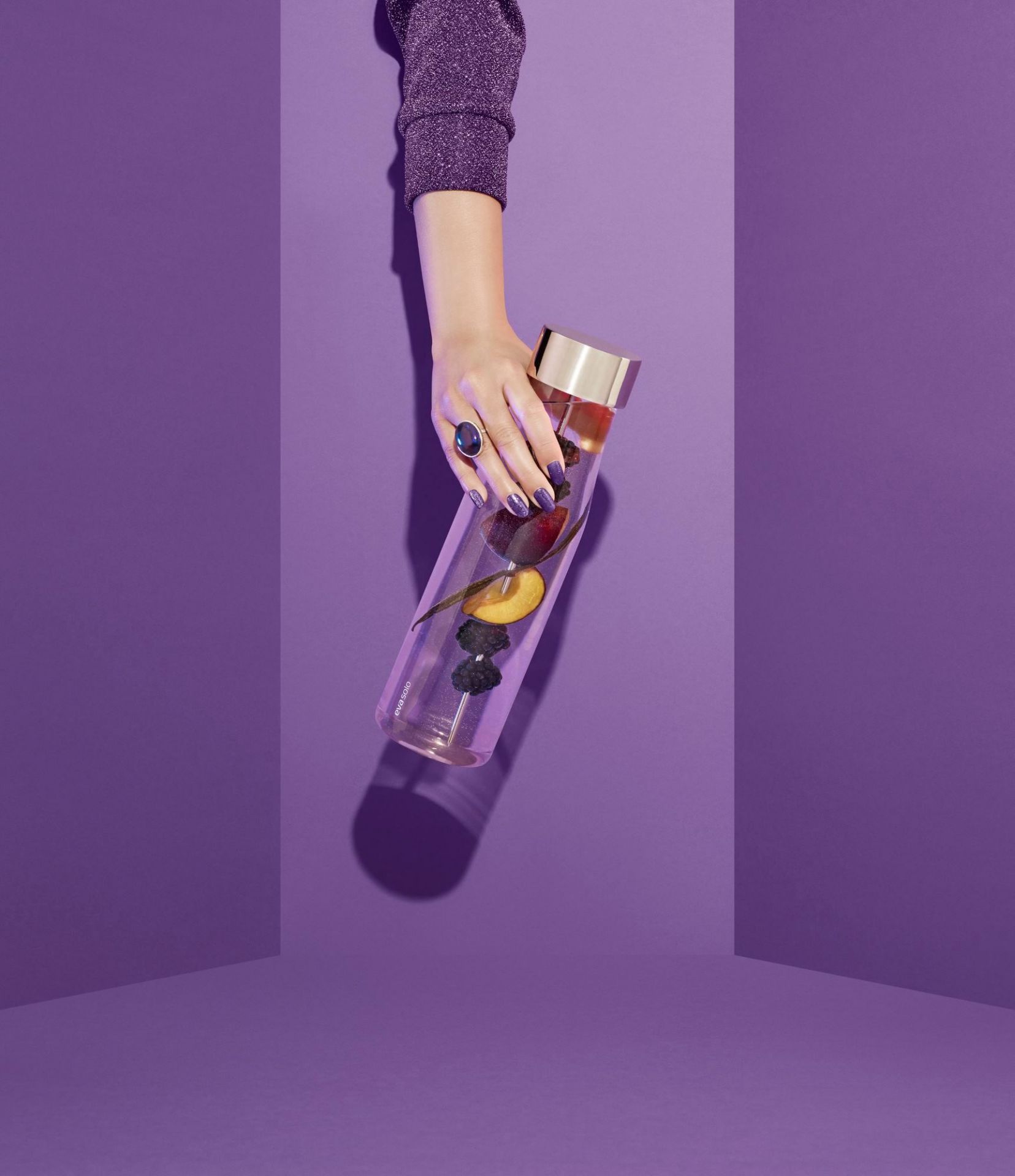 Hand hält My Flavour Karaffe von Eva Solo, gefüllt mit Früchten, vor lila Hintergrund.
