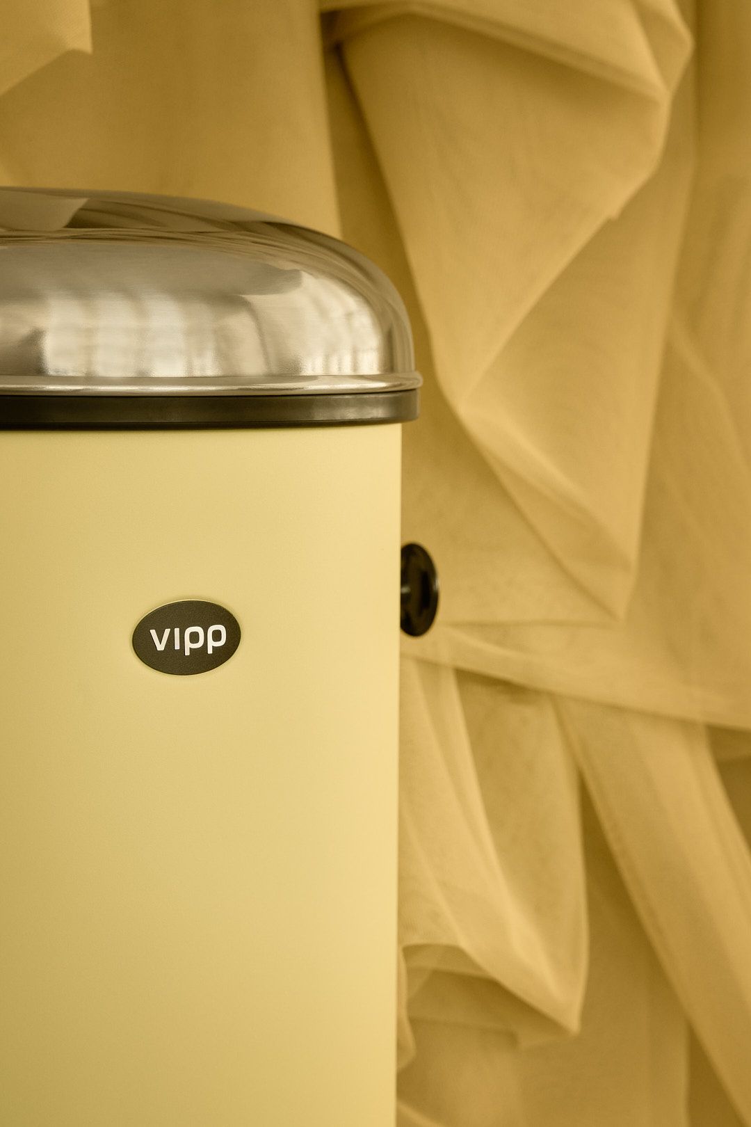 Nahaufnahme des gelben Marie´s Vipp Treteimers mit Edelstahldeckel vor einem gelben Stoffhintergrund.