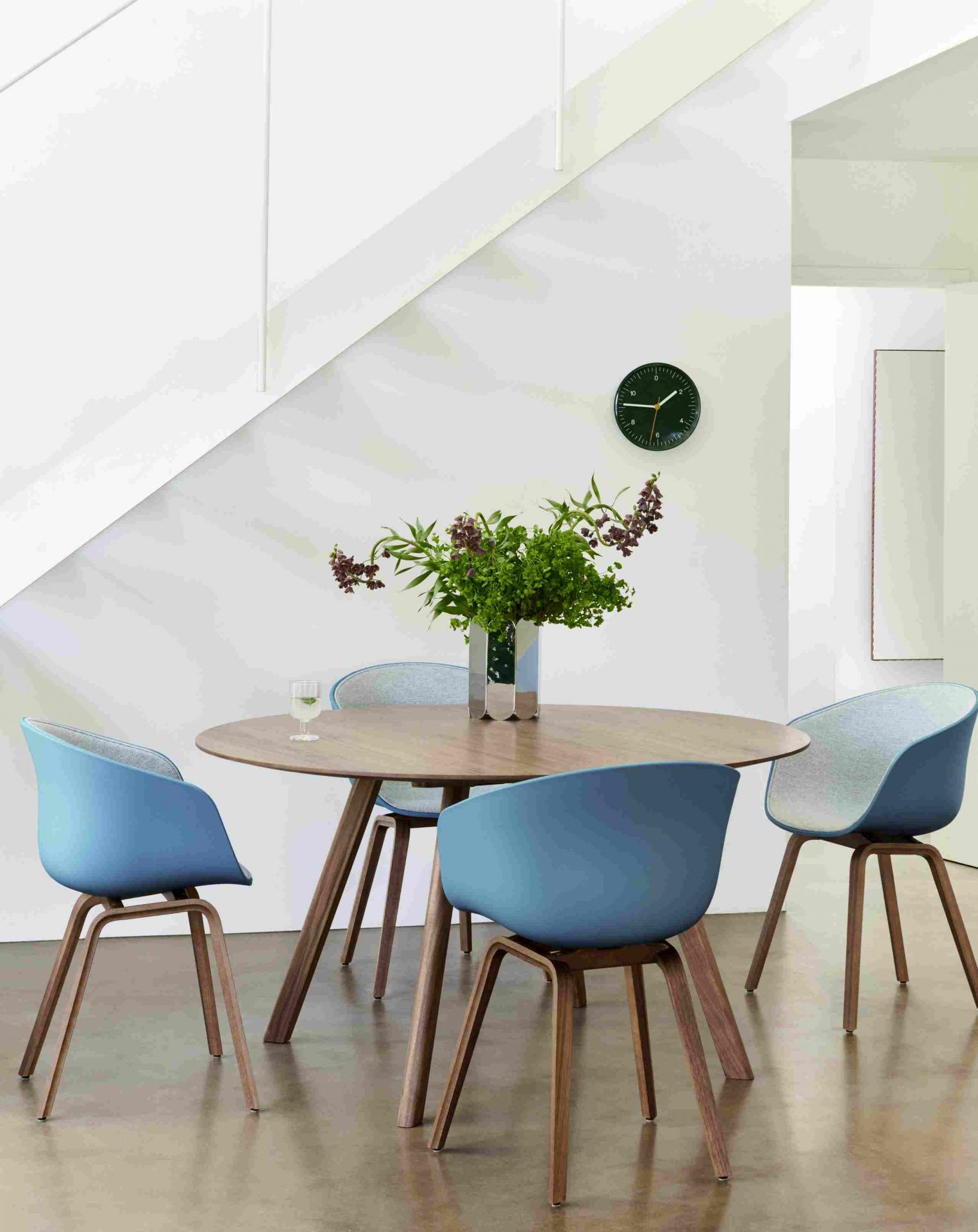 Heller Essbereich mit rundem Holztisch, blauen Stühlen und Hay Arcs Vase Mirror mit Blumen.