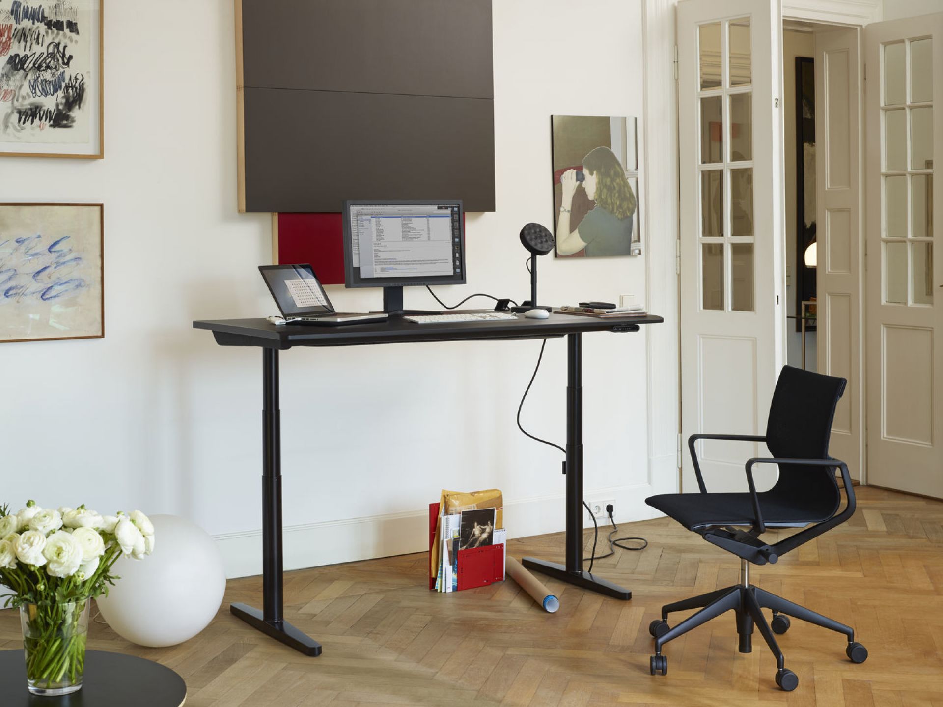 Schwarzer Physix Studio Bürodrehstuhl von Vitra neben höhenverstellbarem Schreibtisch in modernem Büro mit Kunst.