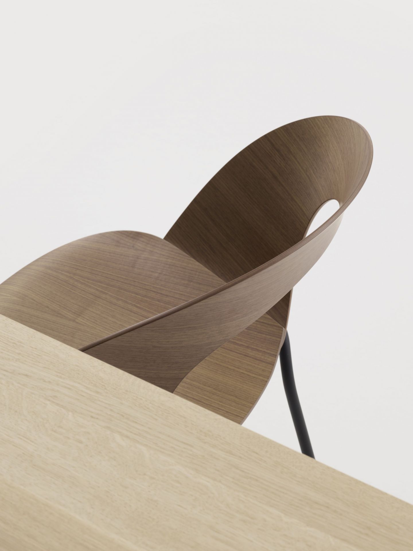 Detailaufnahme des Brunner Mudra Stuhls aus Holz mit schwarzem Metallgestell neben einem Holztisch.
