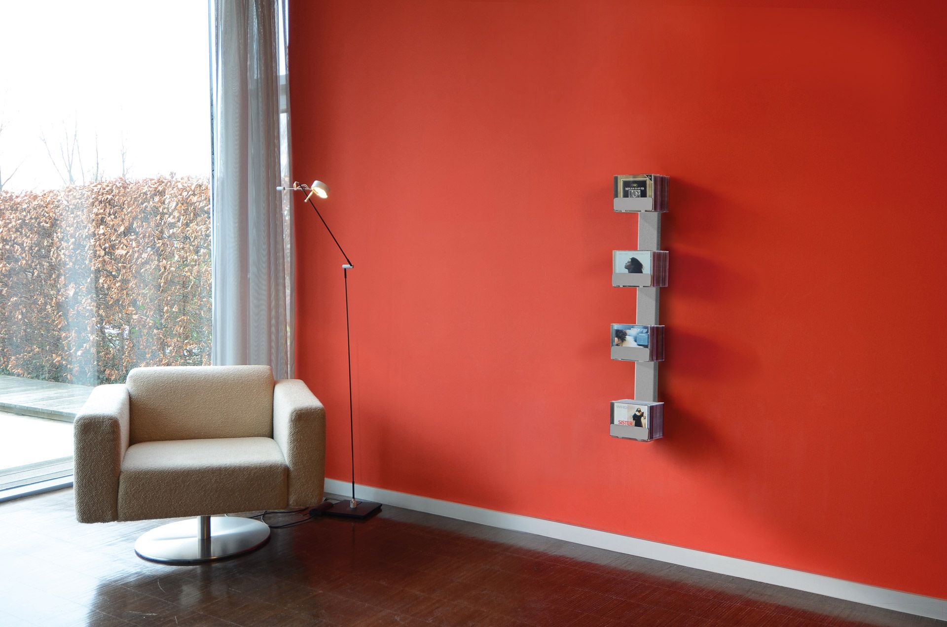 CD-Baum Wandregal: Vertikales Regal für CDs an roter Wand, neben Sessel und Stehlampe.