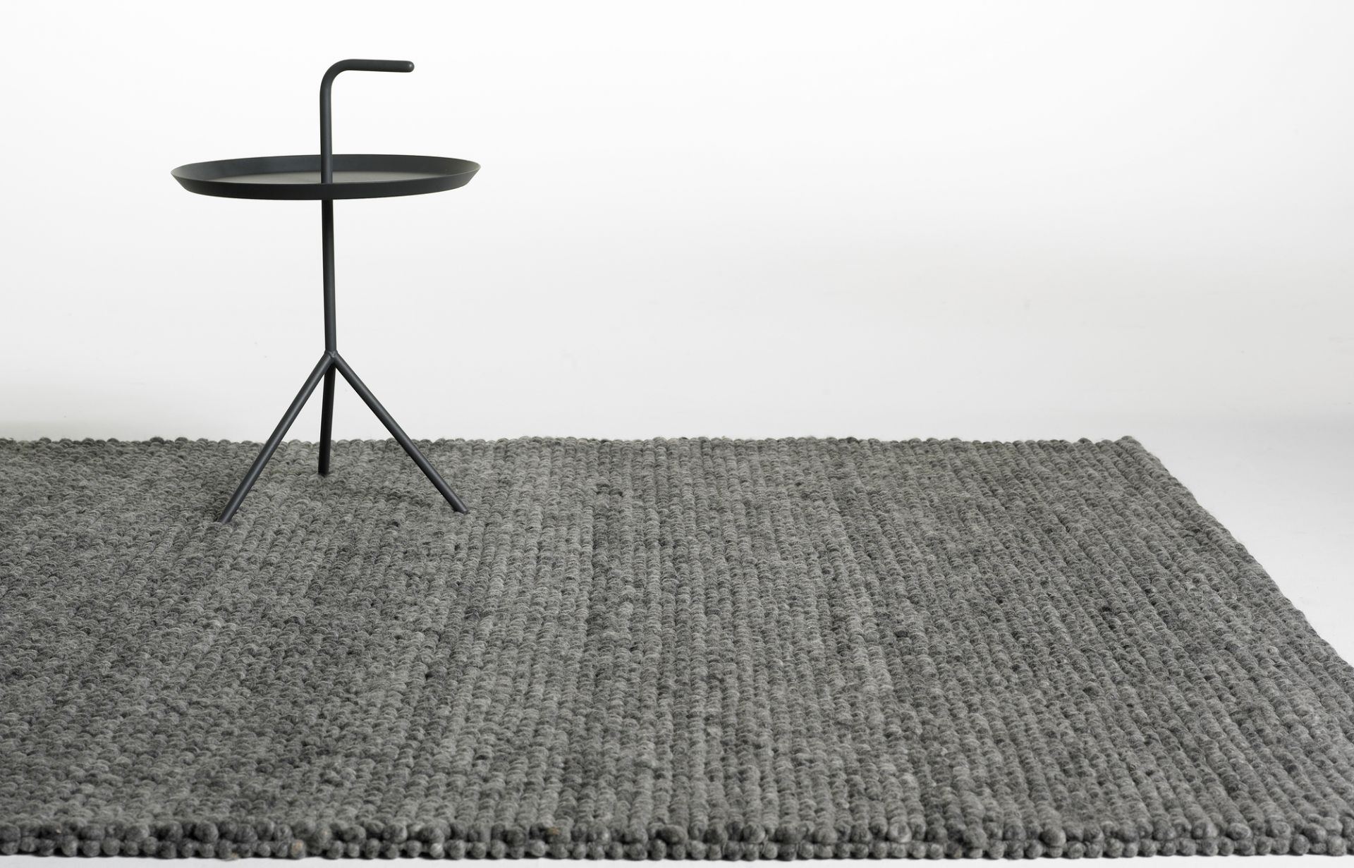 Grauer Hay Peas Teppich (300x200 cm) mit schwarzem Beistelltisch auf weißem Hintergrund.