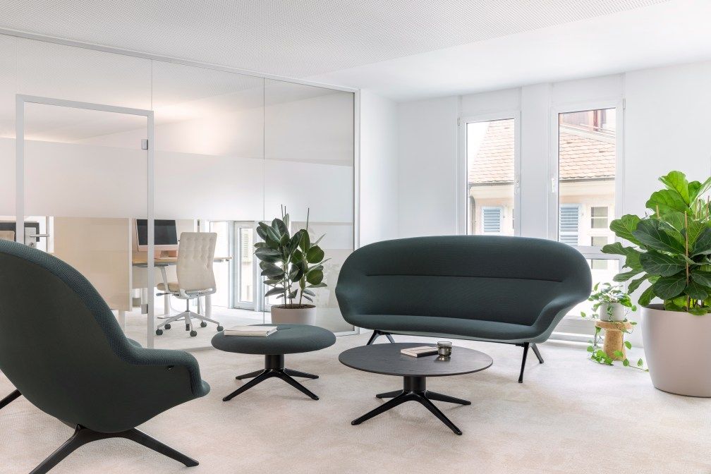 Abalon Sofa von Vitra in modernem Büro-Lounge-Bereich mit Sessel, Tisch und Pflanzen.