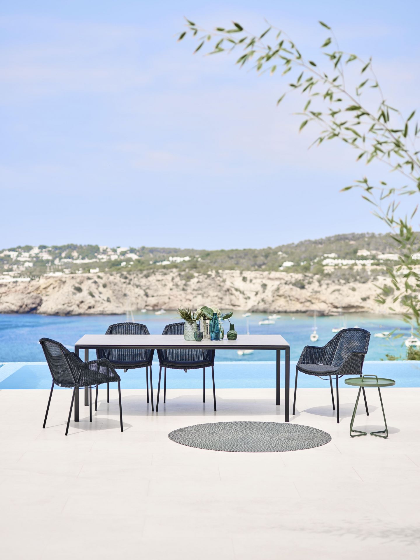Cane-Line Pure Outdoor Esstisch mit Stühlen auf einer Terrasse mit Meerblick, stilvolle Gartenmöbel.